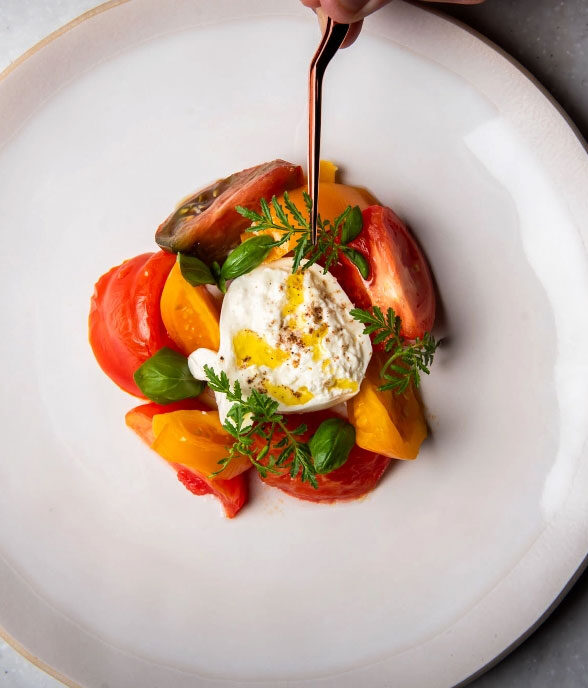 Burrata over heirloom tomatoes with basil and olive oil, served on a wide white plate