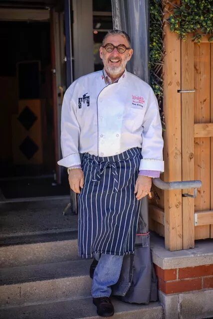 Chef Mark Kitching in white chef’s whites and a striped apron, standing in the doorway of Waldo’s on King