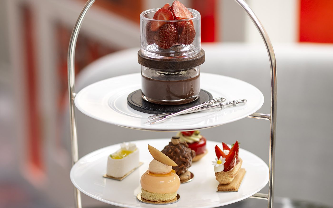 A two-tier dessert stand with a glass of strawberries over chocolate pot de crème above a plate of petits fours &mdash; passionfruit slice, caramel dome, chocolate feuilletine and strawberry tart
