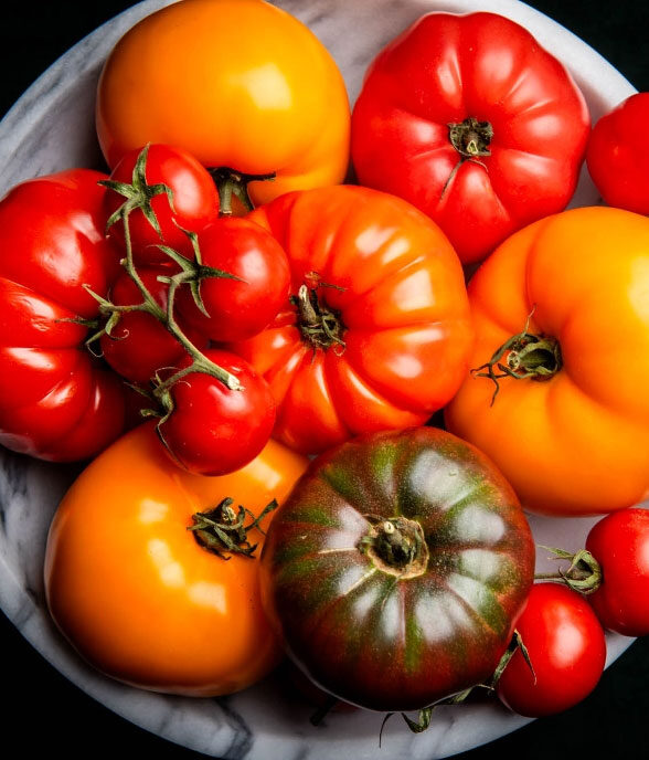A marble bowl of heirloom tomatoes in red, orange, yellow and green