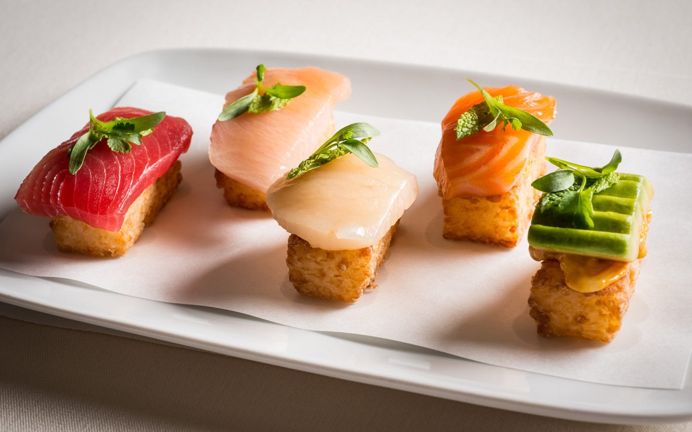 Five crispy rice bites topped with tuna, hamachi, scallop, salmon and cucumber, finished with micro herbs and set on a white platter