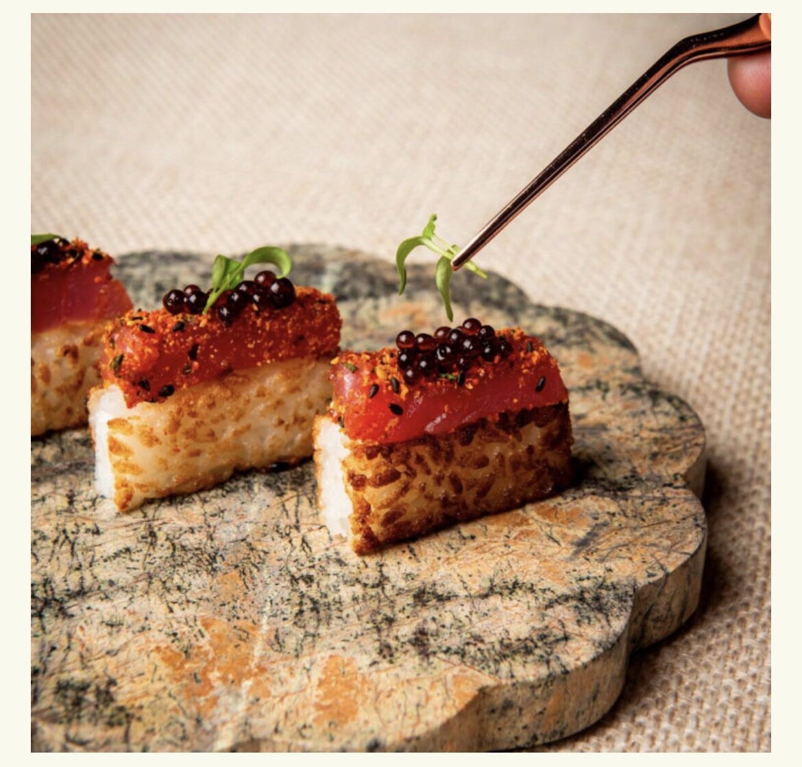 Crispy rice bites topped with seared tuna and pearls of caviar, finished with tweezers on a marble board