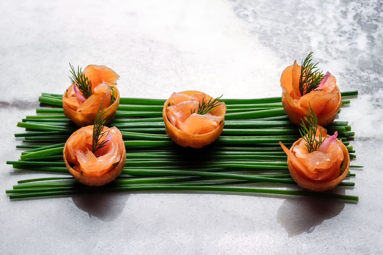 Smoked salmon canapés in crisp tartlet shells, arranged in a row over a bed of fresh chives