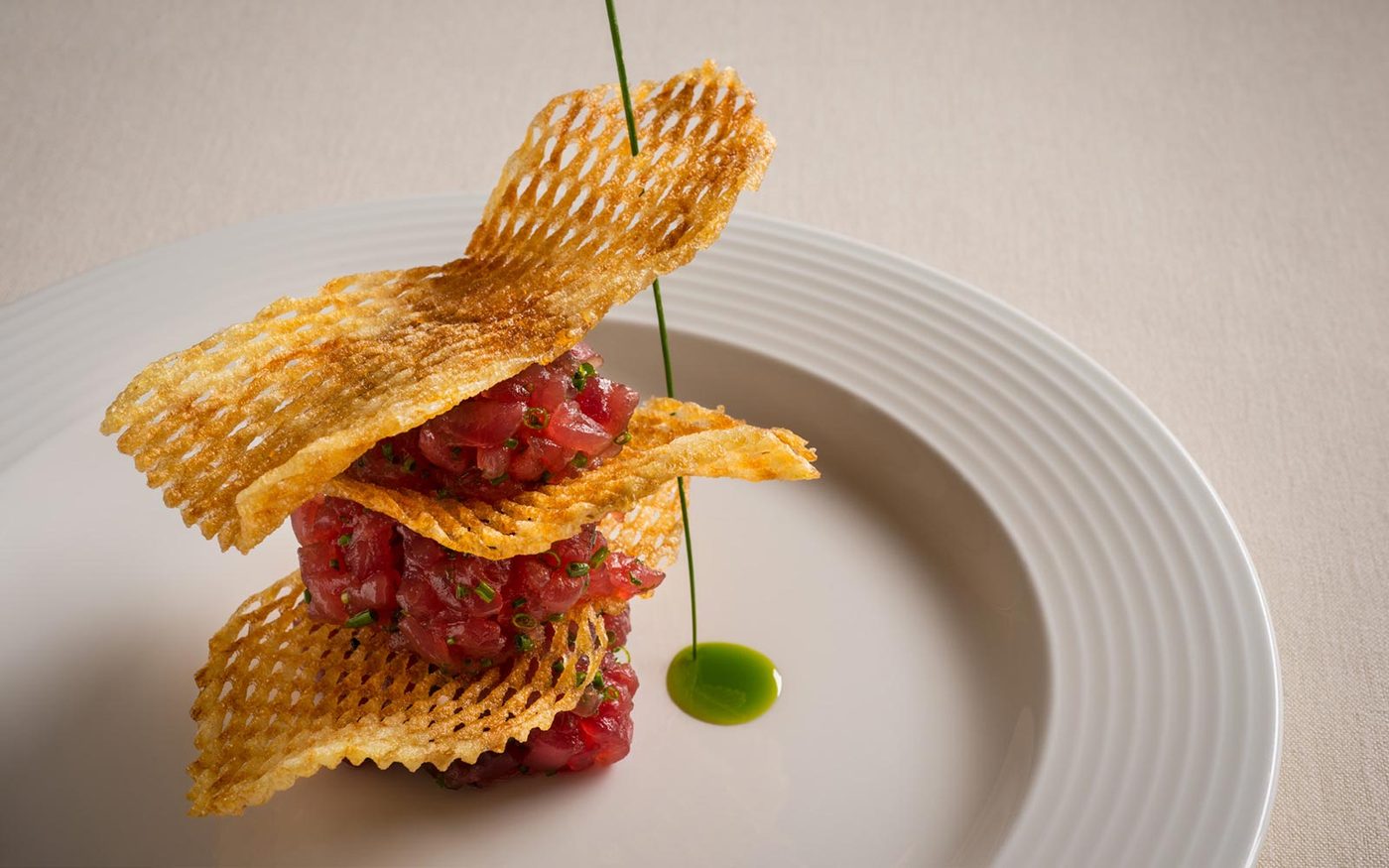 A tower of chive-flecked tuna tartare layered with lattice potato crisps, finished with a drop of herb oil