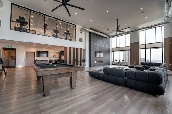 A double-height lounge with deep sectional seating, a billiards table, a bar and a two-storey wall of windows