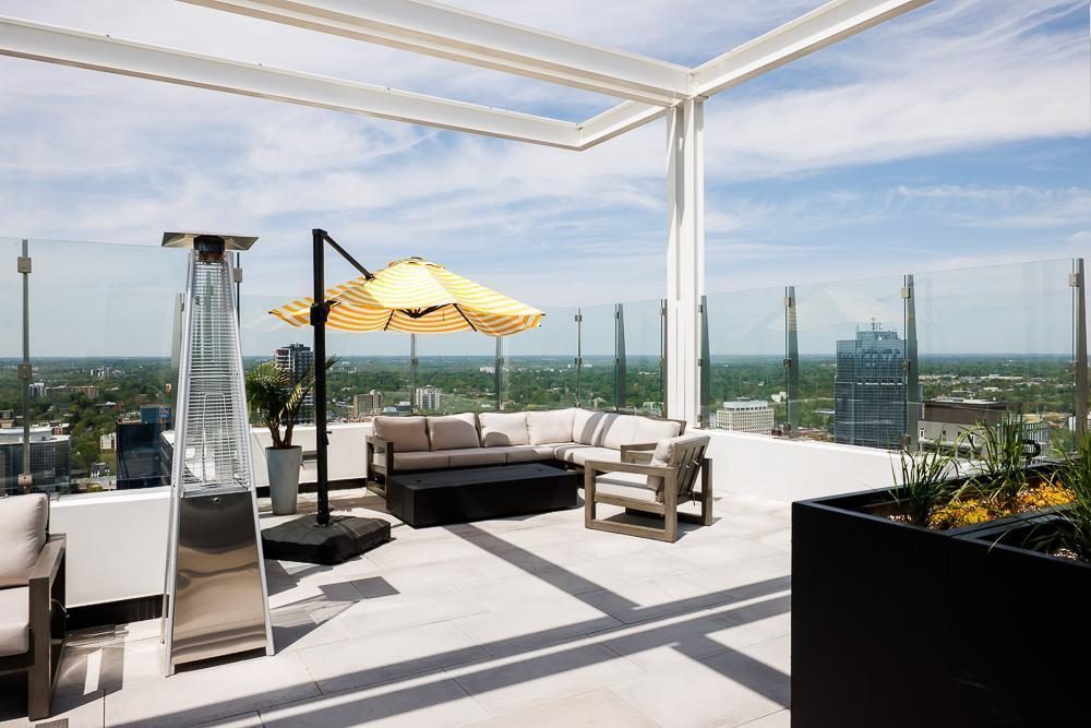A rooftop terrace with a white pergola, sectional lounge seating, a patio heater, planters and a yellow-striped umbrella, opening onto the London skyline