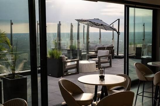 A rooftop terrace with lounge seating, planters and a cantilevered umbrella, opening onto a city skyline at dusk